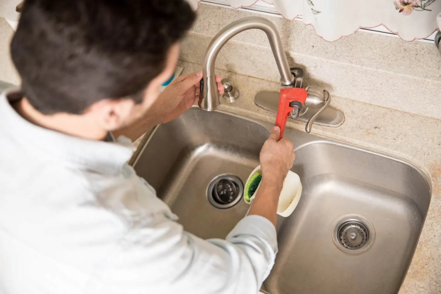 Plumber fixing a kitchen faucet with a pipe wrench